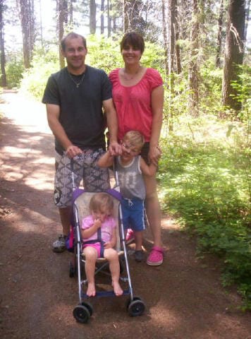 Family of 3 walk along a trail with trees in warm weather