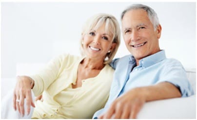 A couple with grey hair sits on a white coach