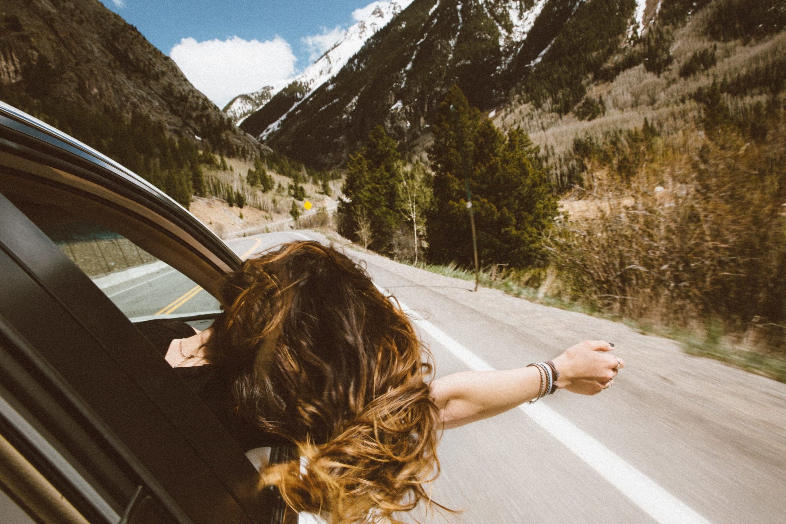 Person hanging out of the car window as car travels along the road