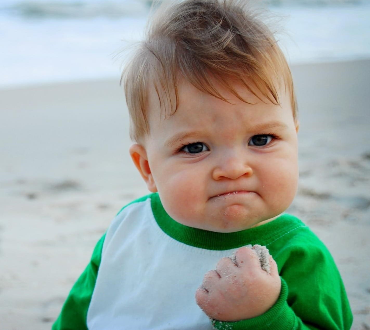 young child makes a fist pump while on the beach