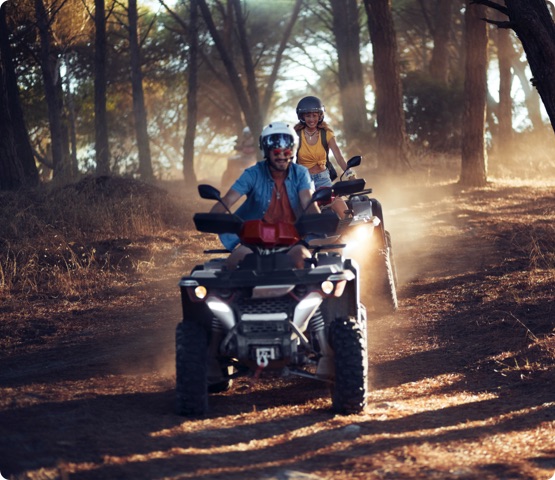 Two people wearing helmets having fun and riding quad bikes in the forest