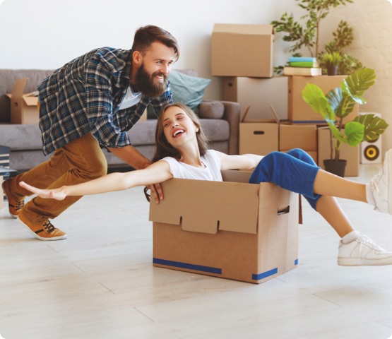 Person sits in empty cardboard box, goofs around with partner in new condo unit