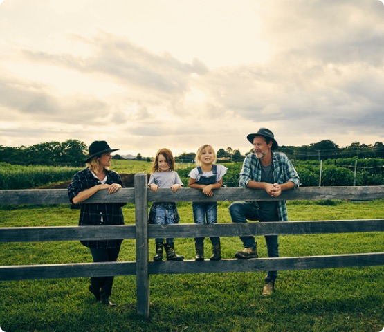 four people leaning against a fence, farm in background