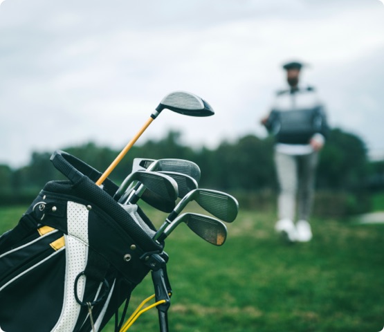 Close-up shot of a golf bag in a golf course. There is an unrecognizable defocused person in background, focus on the golf bag. Horizontal shot.