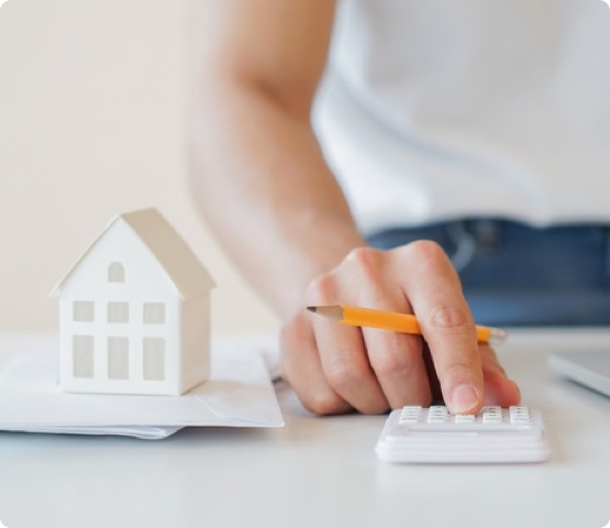 close up of hand using calculator with graphic of house model to indicate person is calculating the home's mortgage or finances