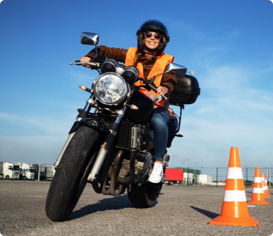 Student wearing helmet taking motorcycle lessons and practicing ride. In background traffic cones and instructor with checklist rating and evaluating the ride. Motorcycle school of driving.