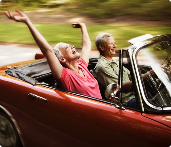 2 smiling people drive in classic car along a roadway
