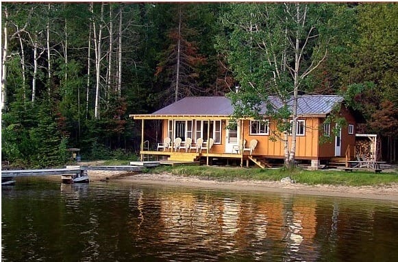 Cottage on the lake with tall trees in backdrop