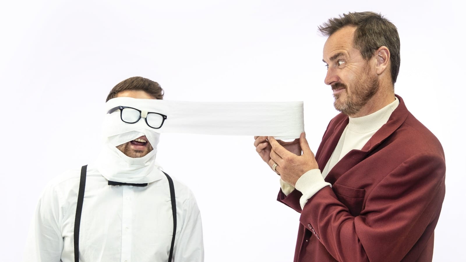 2 people playing around with toilet paper. One wrapping paper around the other person's head, making funny face