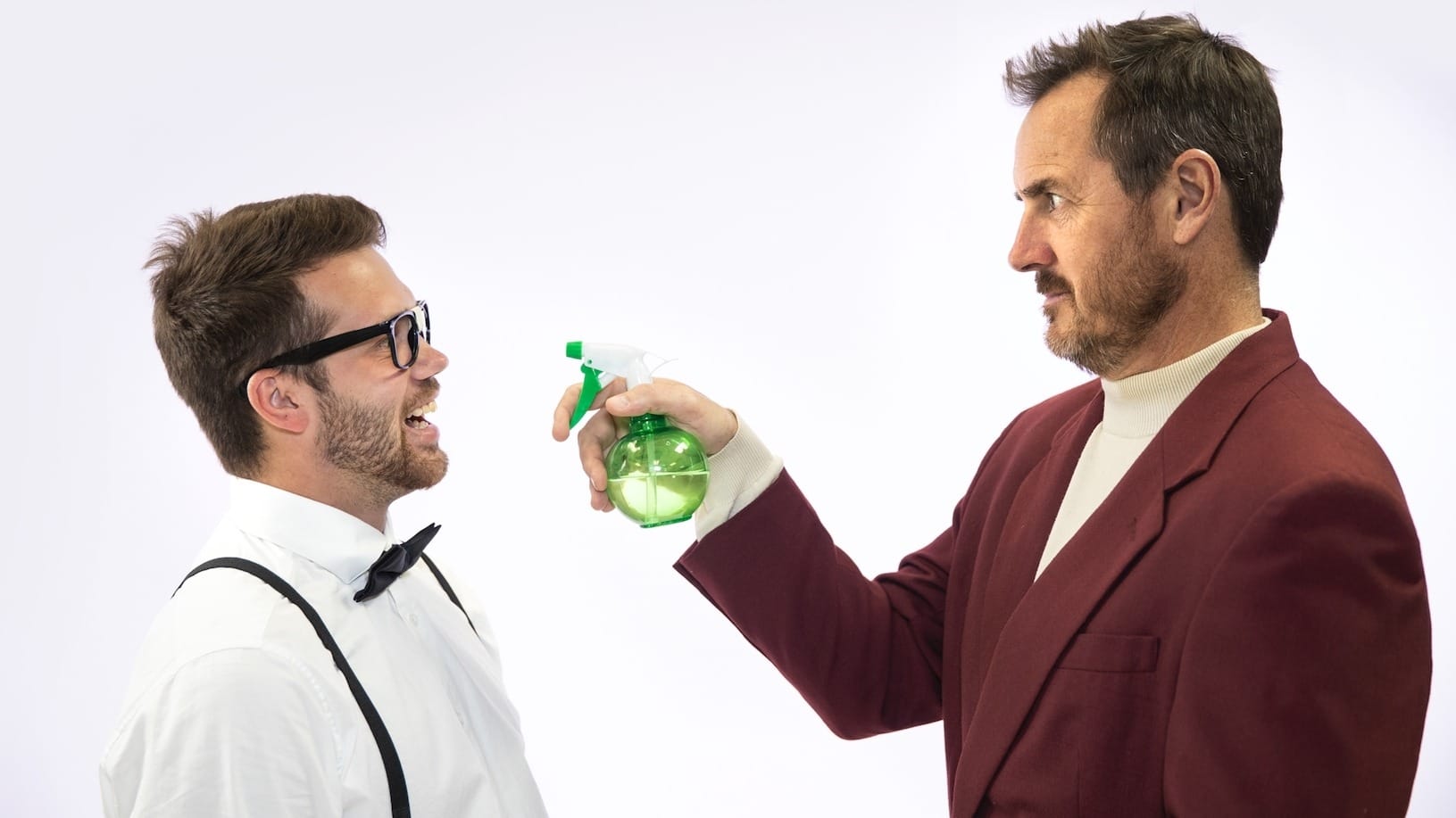 Person holding spray can pointing at another person with glasses, bow tie and suspenders