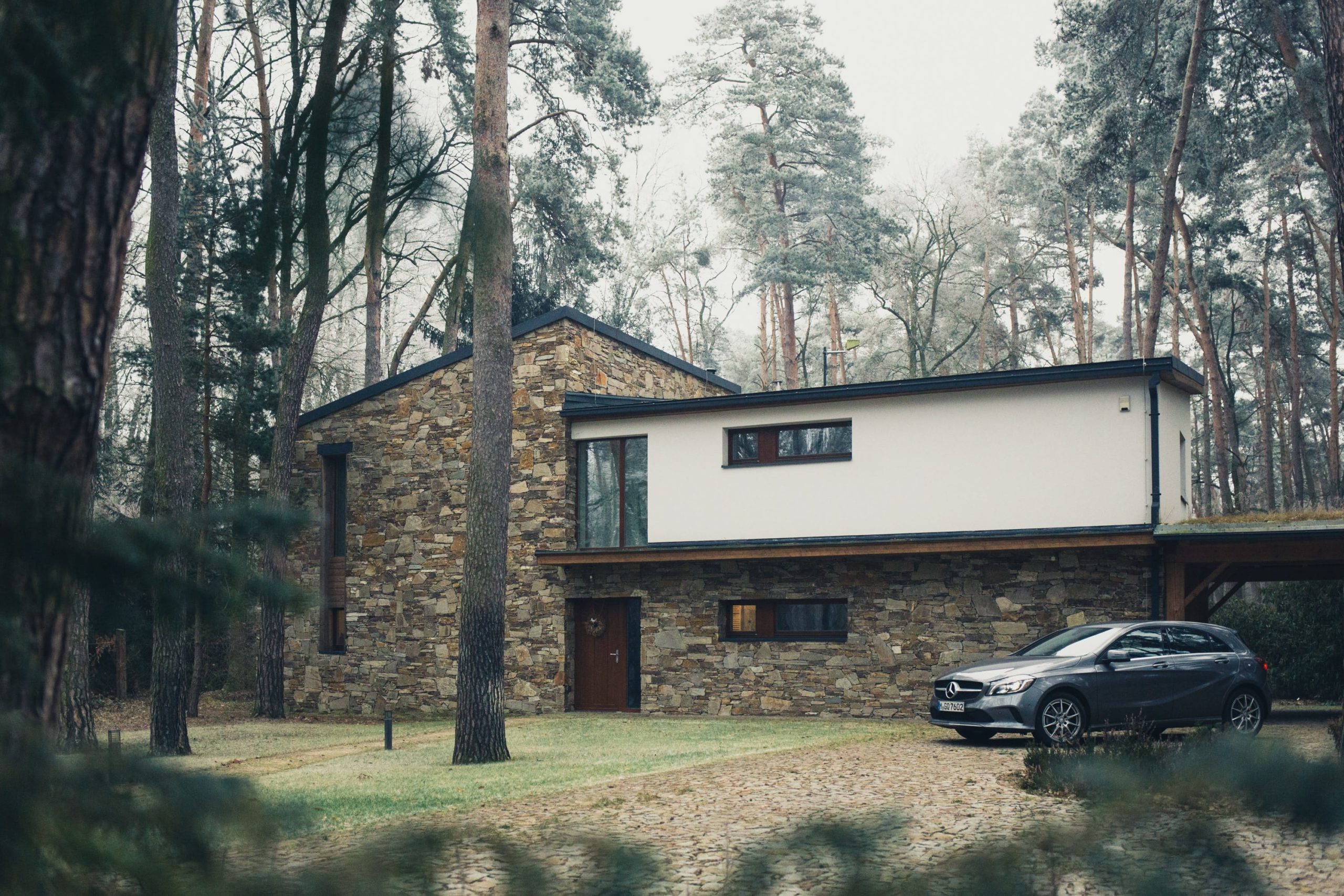 Modern home with car in driveway surrounded by tall trees