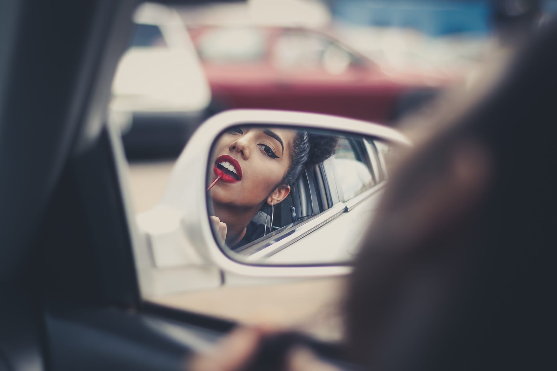 Person applying lipstick using the side mirror of the car