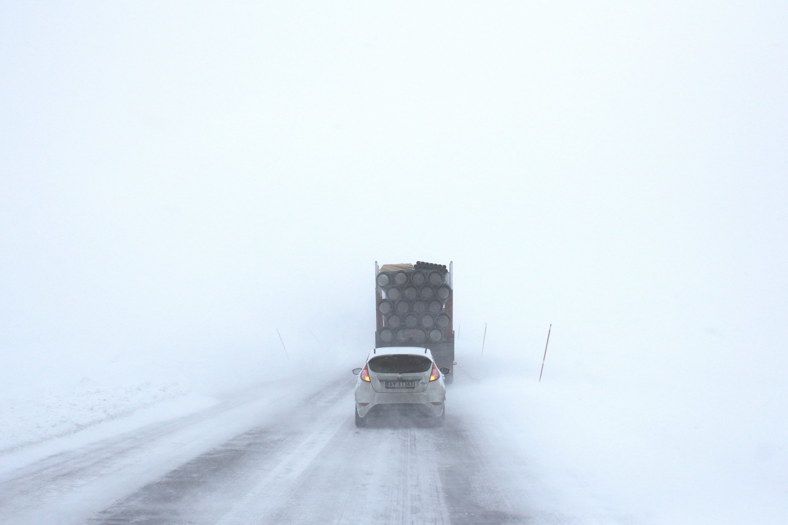 Car travels on the road behind a truck on a snowy day with minimal visibility