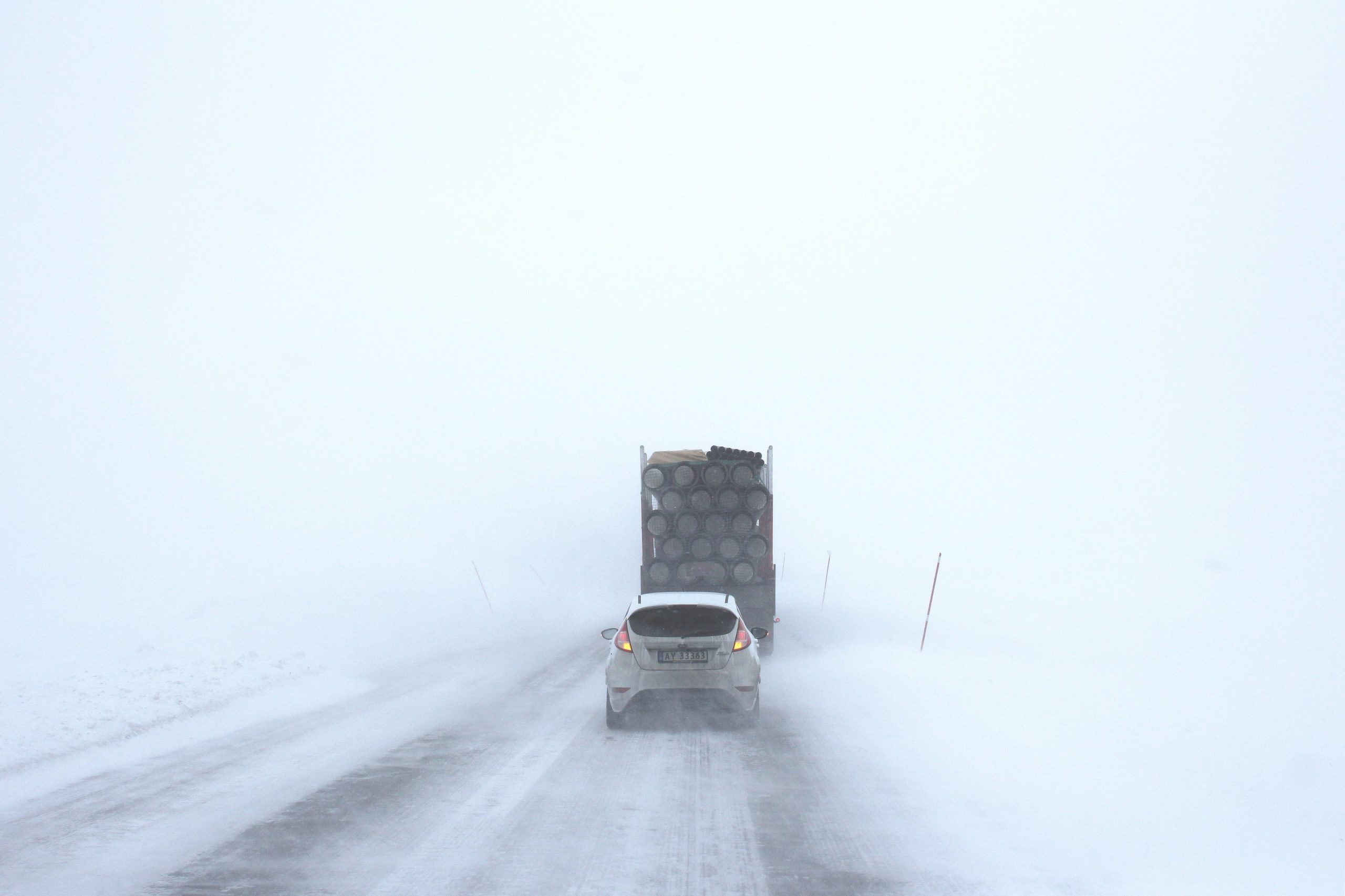 Car travels on the road behind a truck on a snowy day with minimal visibility