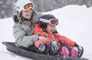 2 kids tobogganing down a snowy hill