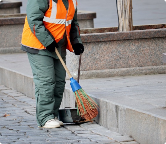 Street cleaning, female municipal worker in uniform sweeping the sidewalk with a broom