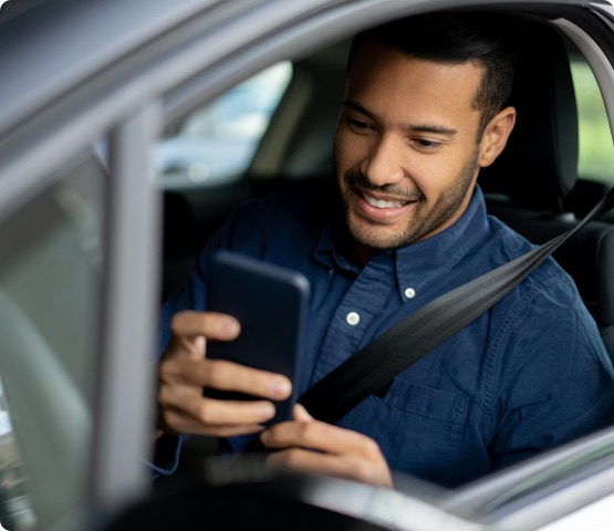 Portrait of a happy man texting and driving in his car on his cell phone