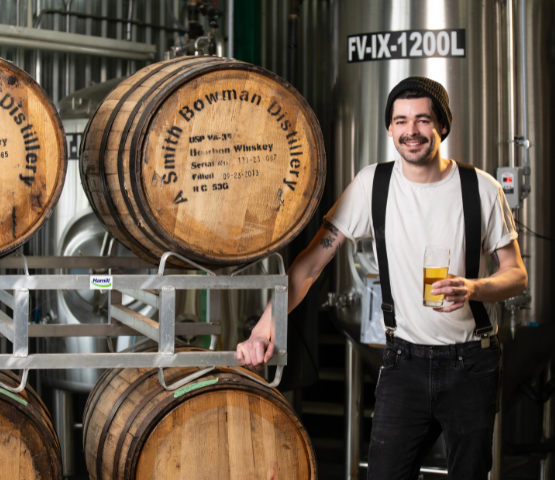 Brewery Insurance with brew master holding beer standing beside aged barrels